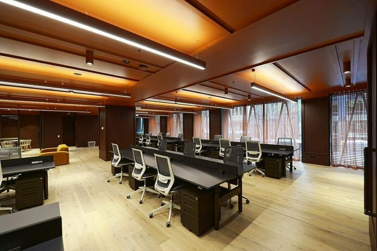 Spacious open-plan workspace at Queen & Collins featuring dark desks and warm overhead lighting.