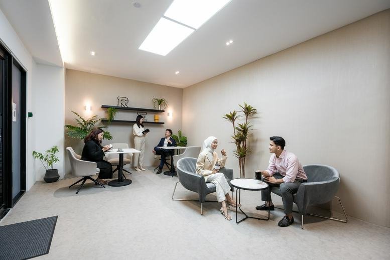 Professionals having a relaxed discussion in a cozy lounge area with comfortable grey armchairs.