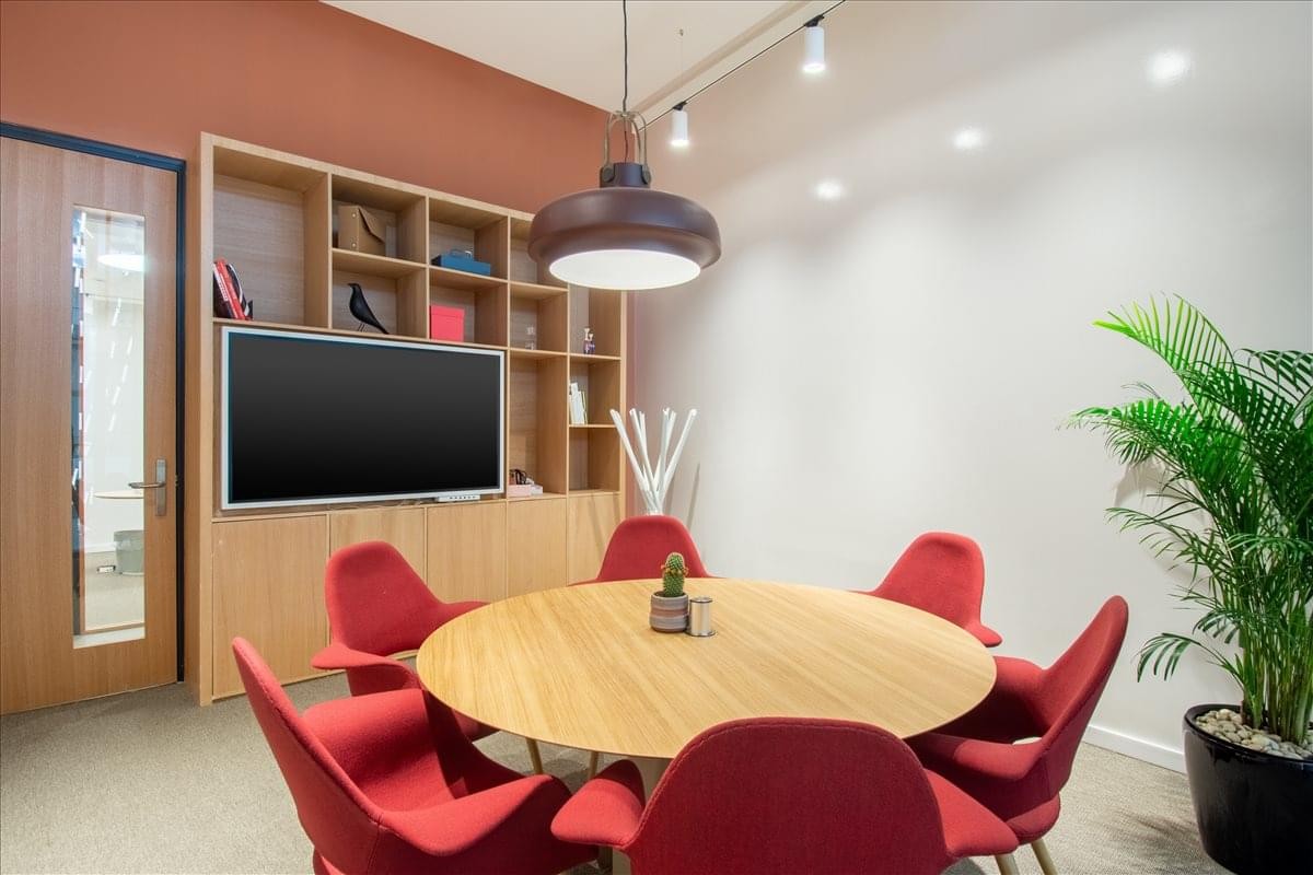 Meeting room at 1st Floor,Riyadh Park, Al Aqiq with a round wooden table, red chairs, and a large wall-mounted screen.