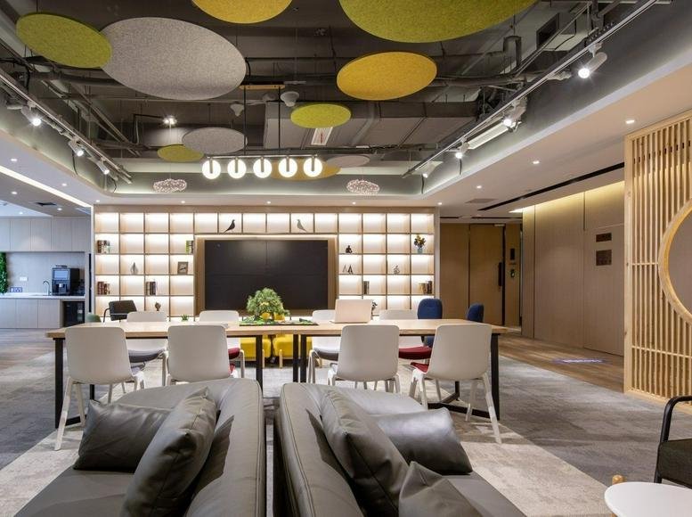 Spacious coworking area at Weilan Business Port with colorful acoustic ceiling panels and a library wall.