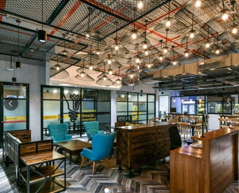 Spacious communal lounge at Sabari Complex with industrial design, exposed ceilings, and warm, hanging light bulbs.