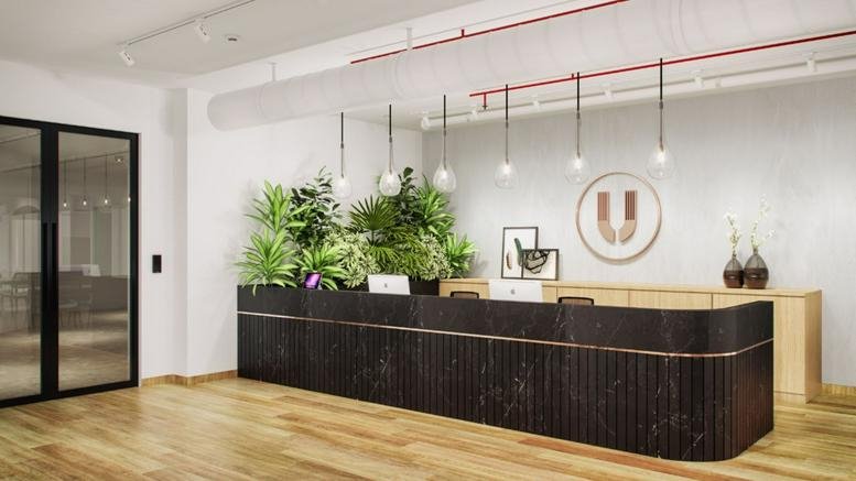 Reception area at Sai Radhe Complex featuring a dark wood desk, green plants, and a circular logo.