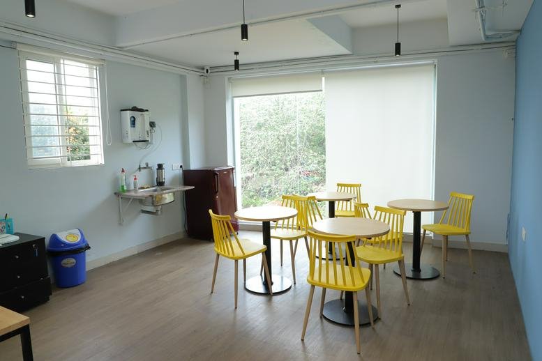 Communal dining area with yellow chairs, round tables, and a kitchenette at Sanjay Nagar Main Road office.