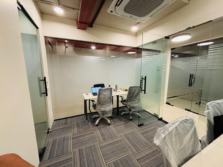 Internal two-person office suite with glass partitions and grey carpeting.