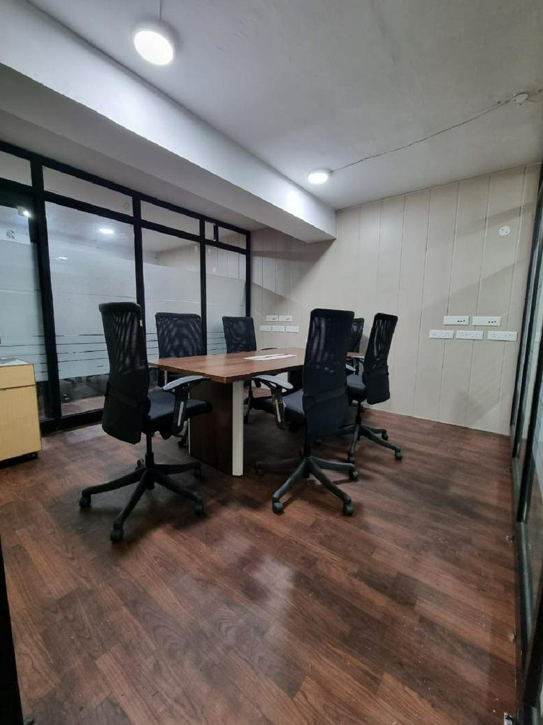 Professional meeting room featuring a wooden table and black mesh chairs on dark wood flooring.
