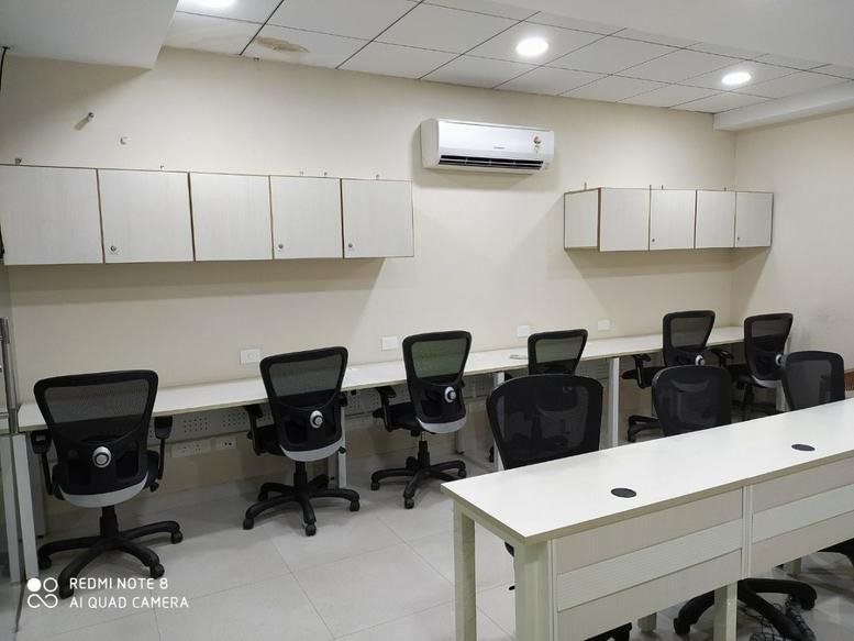 Open-plan workspace with multiple desk rows and white overhead storage cabinets.