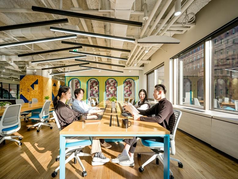 Bright shared workspace with people collaborating at a long table by large windows.