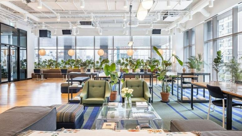 Spacious communal lounge with green armchairs, wooden floors, and numerous potted plants.