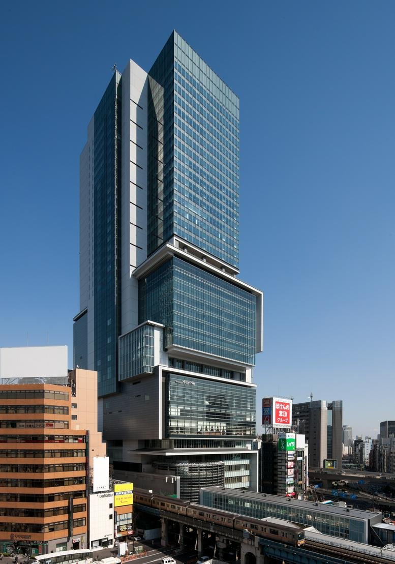 Exterior view of the modern, glass-facade Shibuya Hikarie building against a clear blue sky.