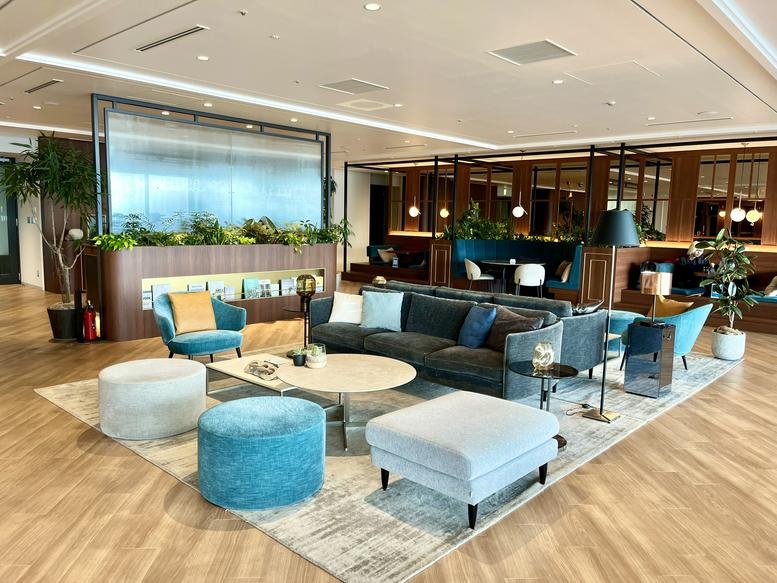 Bright lounge area with colorful velvet armchairs, blue ottomans, and lush indoor plants.