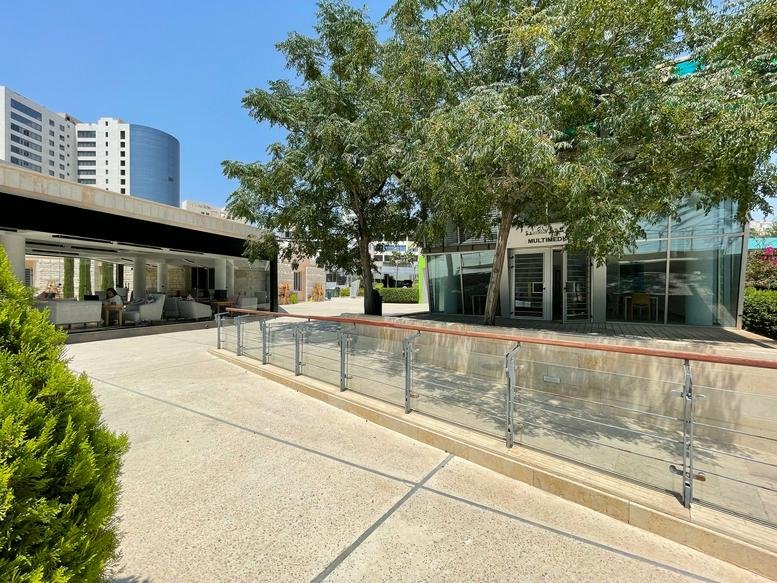 Exterior view of the contemporary HCC building on Prince Shaker Ben Zeid Street featuring glass facades and trees.