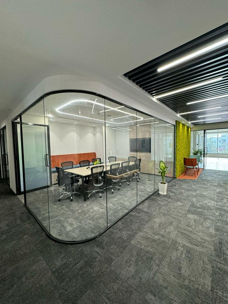 Spacious boardroom enclosed in curved glass walls with grey carpet.