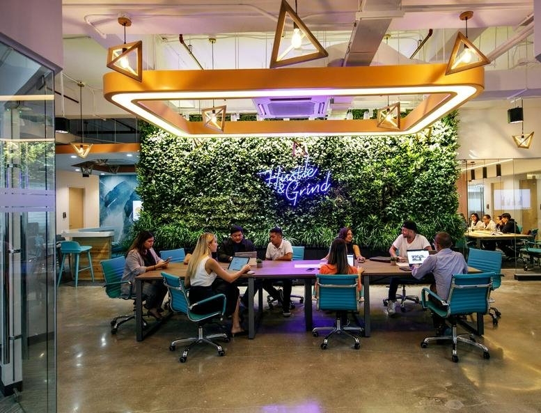 Spacious coworking area with a green wall and a glowing square ceiling light fixture at 1Skyrise 4.