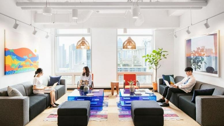 Spacious communal lounge at Spring Tower with blue coffee tables and people working on sofas.