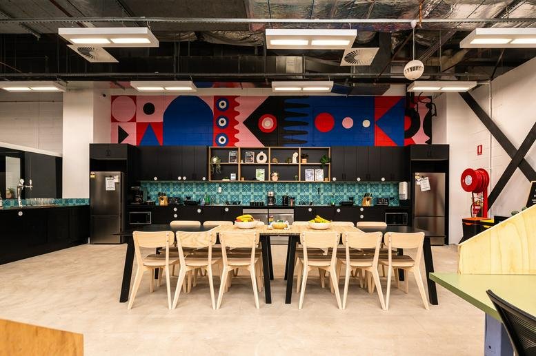 Modern communal kitchen and dining area with a vibrant geometric mural and long wooden table.