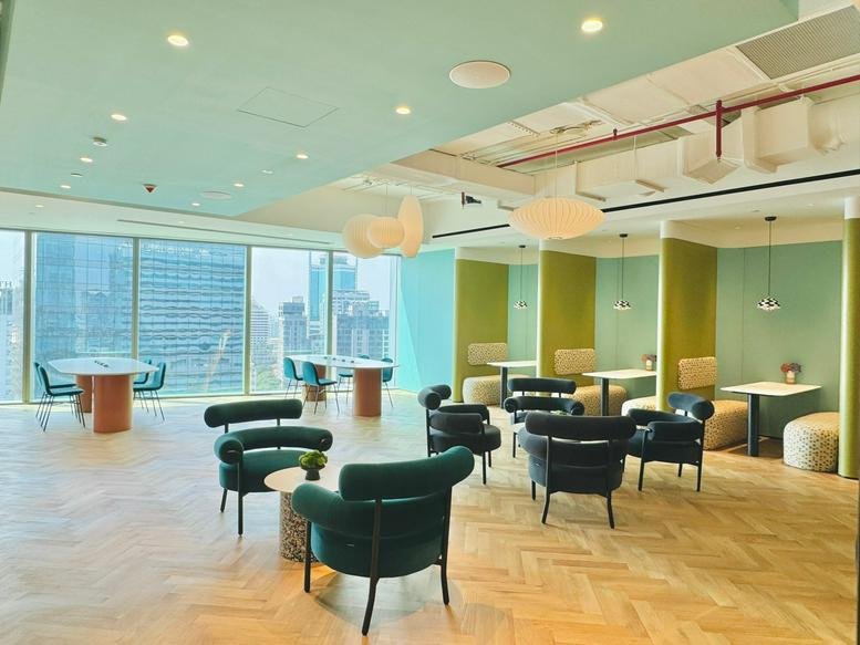 Spacious coworking lounge at The Nexus Tower featuring teal velvet armchairs and city views.