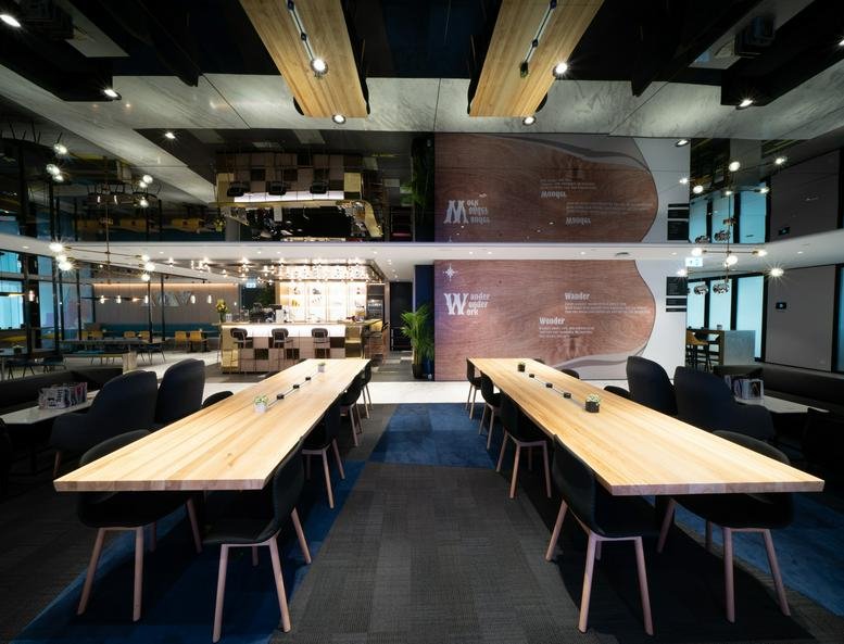 Vibrant two-story communal lounge at Tower 5, The Gateway with long wooden coworking tables.