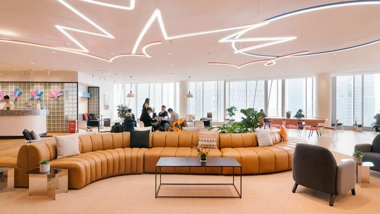 Spacious communal lounge at Trinity Place featuring a large curved tan leather sofa and artistic ceiling lights.