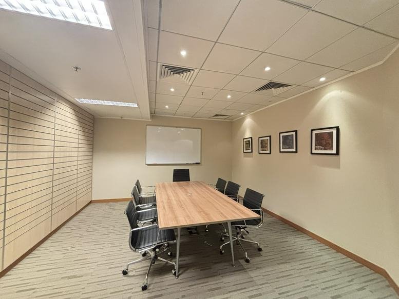 Professional meeting room with a light wood table, black chairs, and framed artwork.