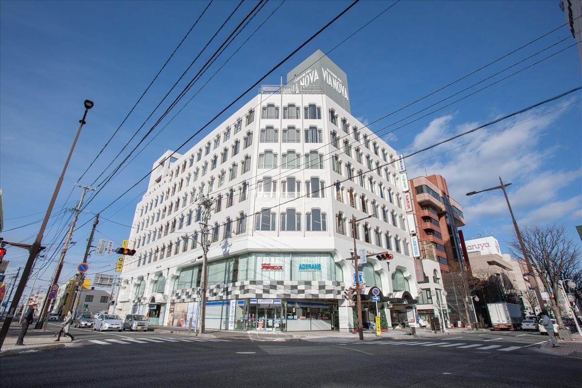 Street view of the multi-story white VIA NOVA Building under a clear blue sky.