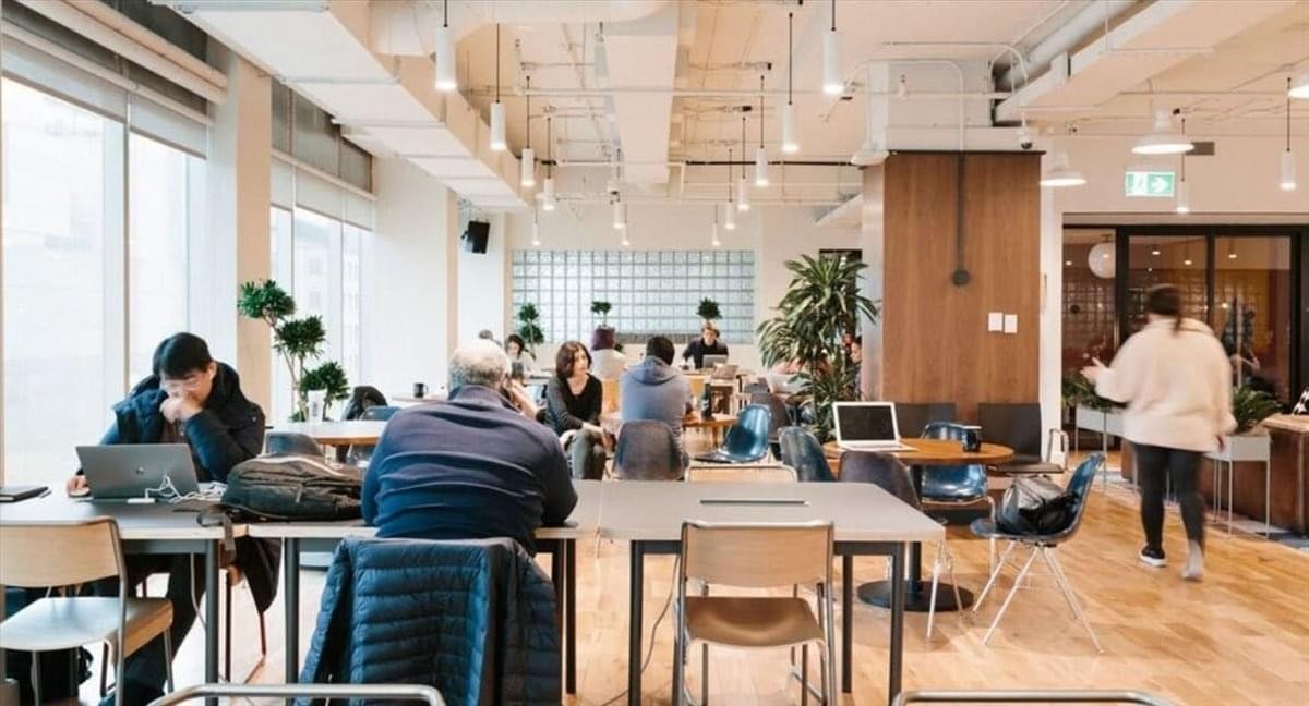 Vibrant communal workspace at WeWork Shinjuku Minamiguchi with long wooden tables and hanging globe lights.