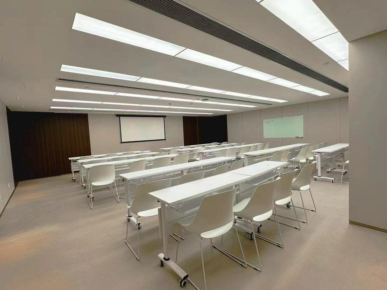 Spacious lecture-style seminar room at the Xinhua Insurance Building with rows of white desks and chairs.