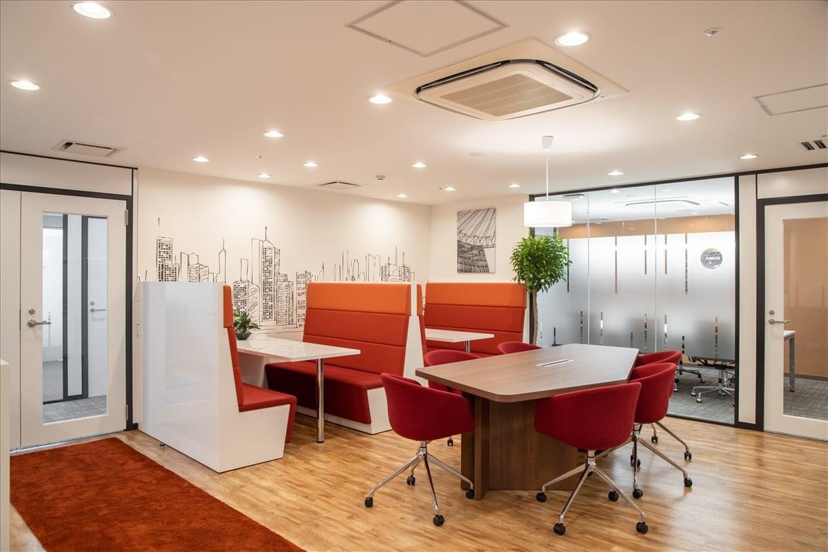 Modern breakout area with red chairs, a long wooden table, and warm lighting at Yamani Building 6F.