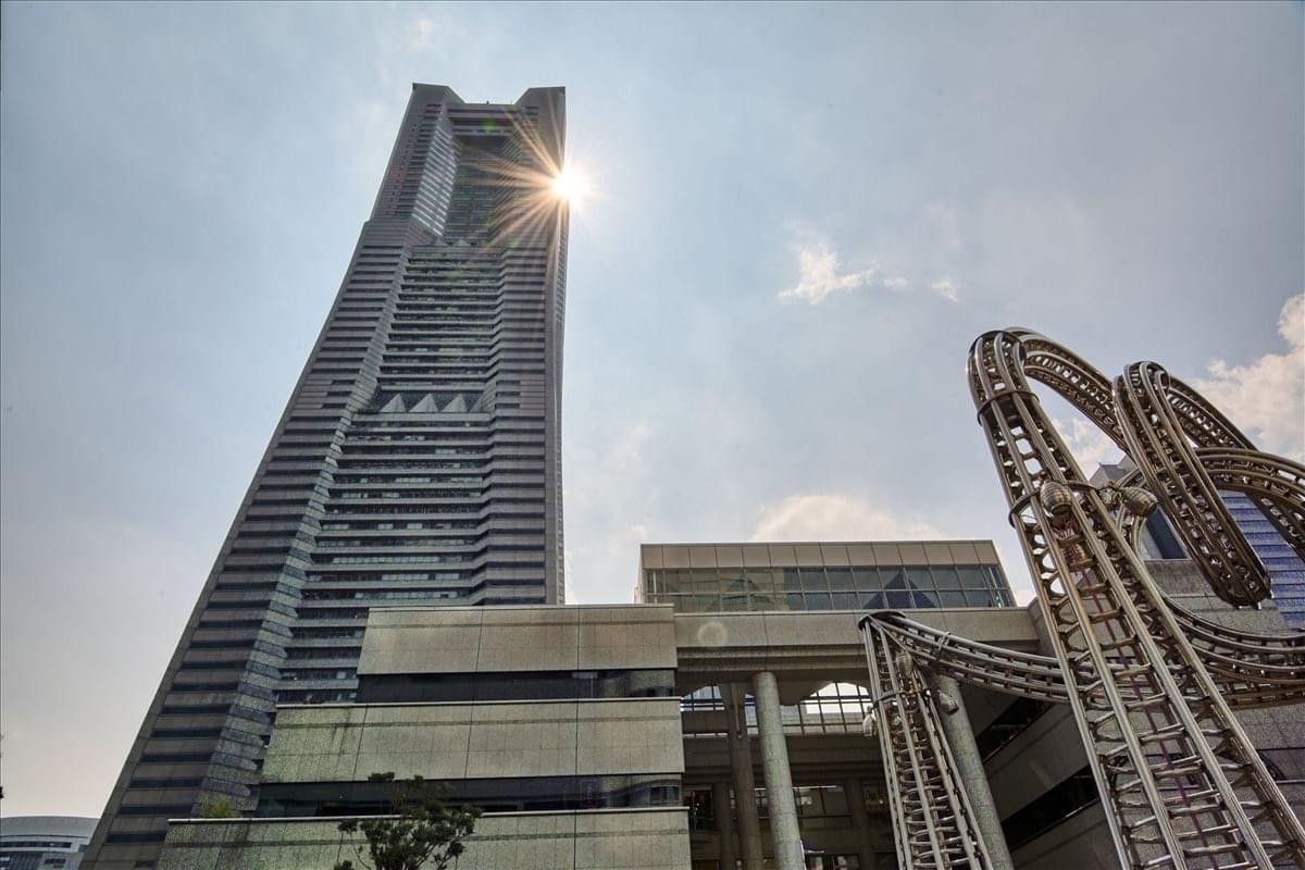 Low-angle exterior view of the sun shining behind the towering Yokohama Landmark Plaza 5F.