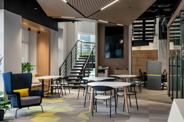 Spacious communal lounge at Sheikh Zayed Road featuring a blue wingback chair, modern tables, and a staircase.