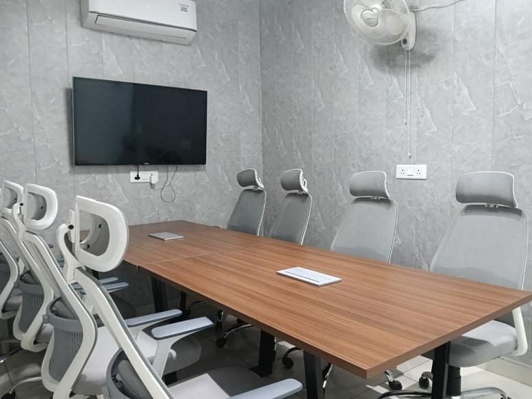 Professional meeting room featuring a wooden table, wall-mounted screen, and grey seating.