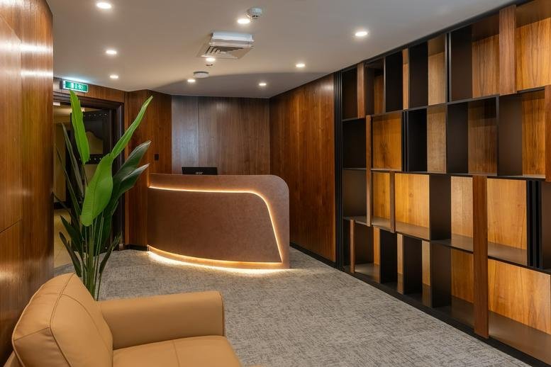 Wooden-paneled reception area at Souk Al Bahar Bridge,AL SAAHA OFFICES BUILDING B with a glowing desk and potted plant.
