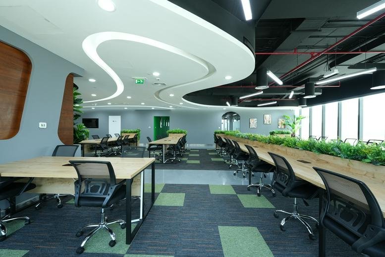 Spacious open-plan workspace at Tamouh Tower with curved ceiling lights and greenery-topped desks.