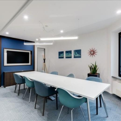 Modern meeting room with a blue accent wall, white table, and teal ergonomic chairs.