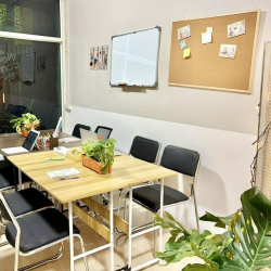 Communal work area with wooden tables, black chairs, and small indoor plants.