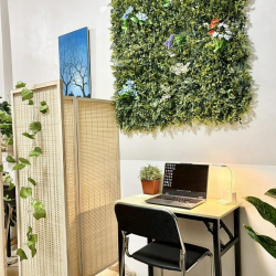 Compact desk area with a laptop and a lush green artificial plant wall.