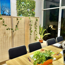 Communal workspace with a long wooden table, laptops, and a lush green feature wall near the window.