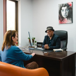 Professional office consultation featuring a man in a hat at a dark wood desk.