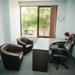 Compact office with a curved desk, ergonomic gaming chair, and twin leather armchairs.
