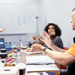 Interactive meeting room with a facilitator using a whiteboard and participants at a table.