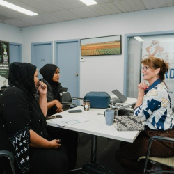 Bright communal workspace with people gathered around tables for a collaborative meeting.