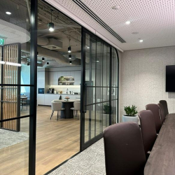 Sleek meeting room with dark chairs and a television, viewed through black-framed glass partitions.