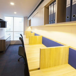 Narrow workspace featuring wooden desks with blue dividers and overhead storage