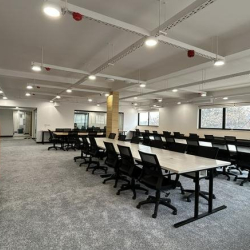 Spacious open-plan coworking area with long rows of white desks and professional black chairs.