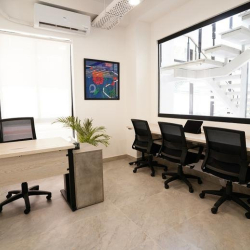 Clean interior office with desks and chairs positioned near a large glass window overlooking a stairwell.