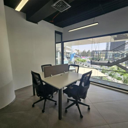 Bright office room with desks and wide city views through glass walls.