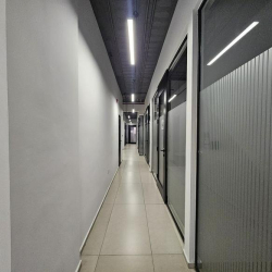 Narrow hallway with glass office partitions and bright lighting.