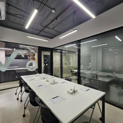 Meeting room with white tables and black chairs, featuring glass walls.