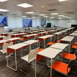 Training room featuring rows of white desks and pops of color from bright orange chairs.