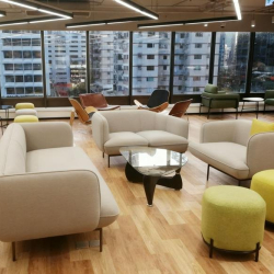 Sunlit lounge area with comfortable cream sofas and yellow stools overlooking the city.