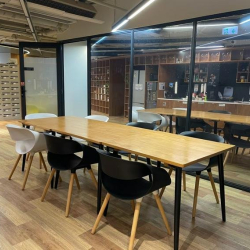 Spacious common area featuring a long wooden table and glass-walled meeting rooms.